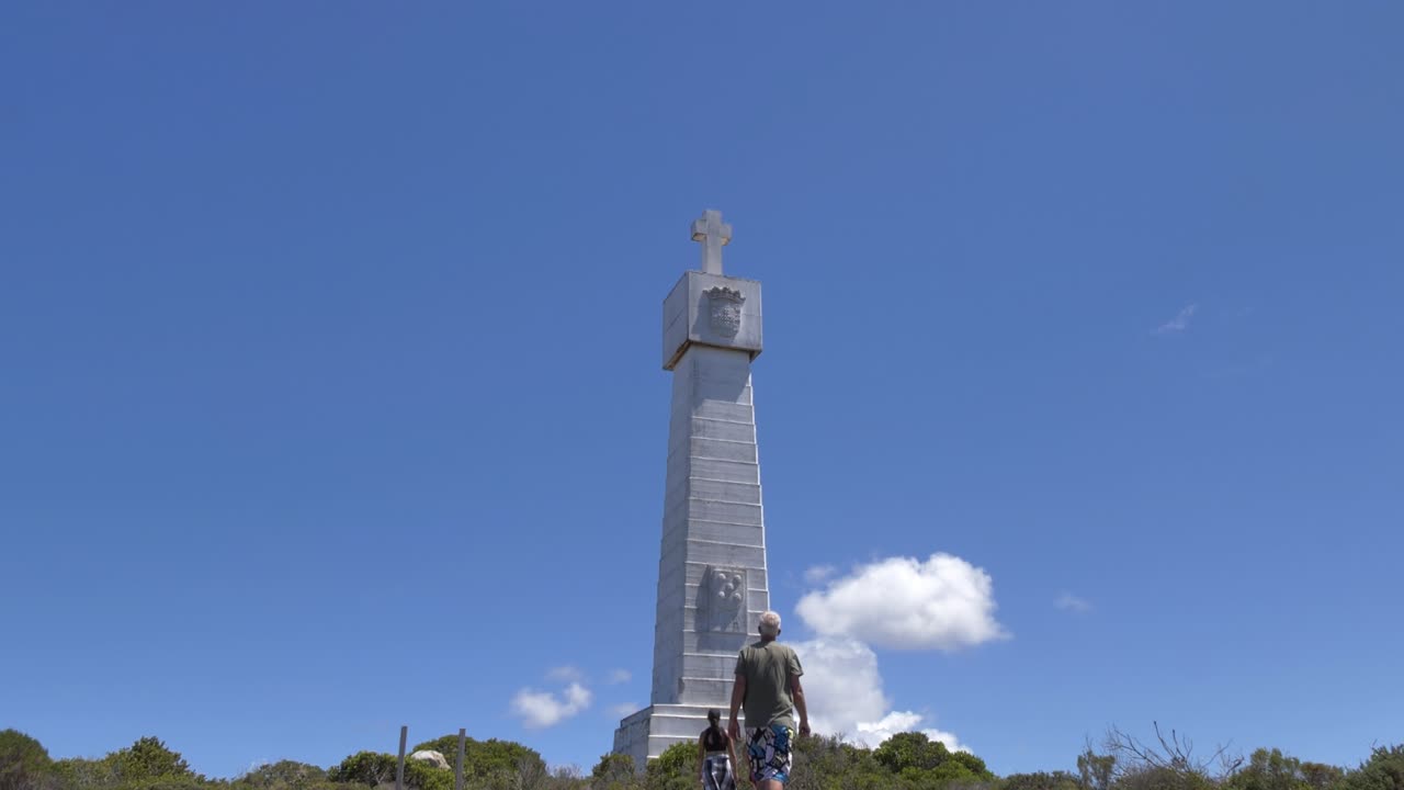 Una vista panoramica della Dias Cross, un monumento prominente, a Cape Point, Riserva Naturale di Cape Point, con alcune persone che si avvicinano in una giornata di sole.
