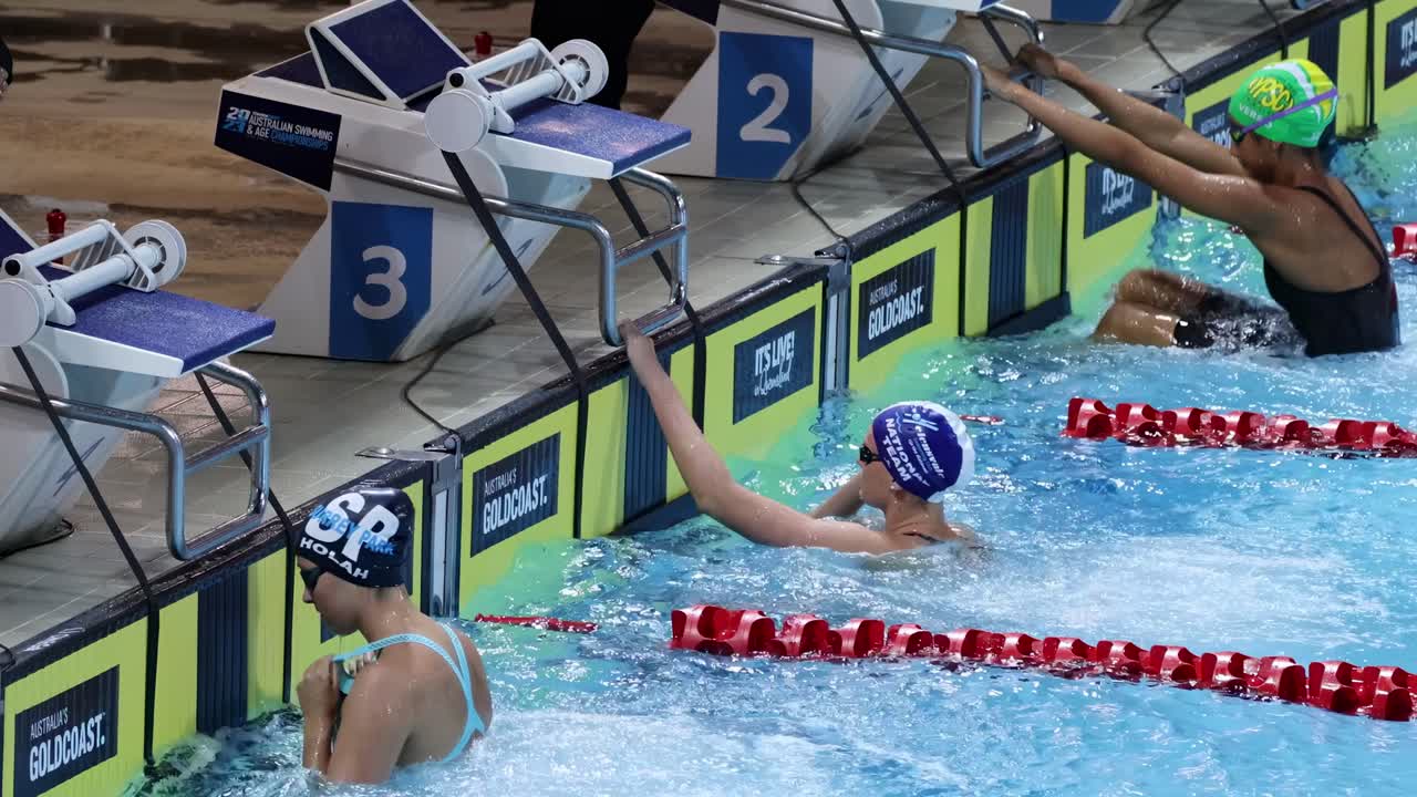 Athletes in swim caps and goggles ready for a backstroke event at the pool's edge.