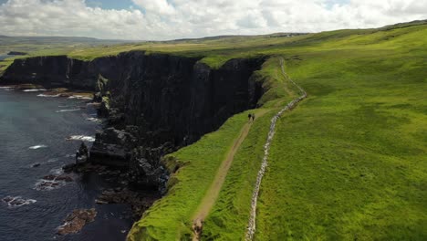 hikers trekking along cliffs of moher coastal hiking trail, aerial follow