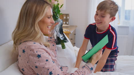 hijo amoroso sorprendiendo a la madre en la cama con flores y tarjeta casera en el cumpleaños o el día de la madre