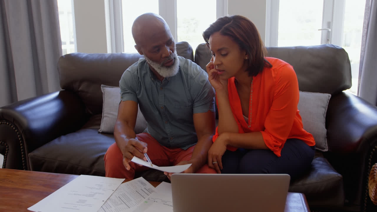 Front view of mature black couple sitting on the couch and discussing bills in a comfortable home 4k