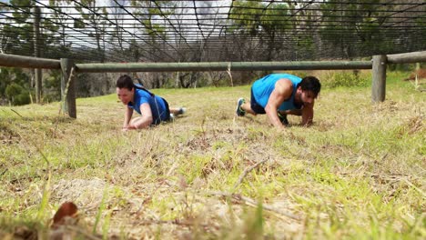 Fit-man-and-woman-crawling-under-the-net-during-obstacle-course