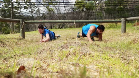 fit man and woman crawling under the net during obstacle course