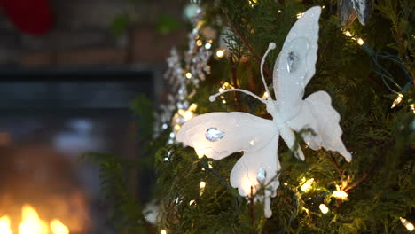 árbol-De-Navidad-Decorado-Con-Luces-Y-Adornos-De-Mariposas---Vista-De-Rotación-De-Paralaje-Cercana-Al-Fuego-De-Cámara-Lenta-En-La-Chimenea-En-El-Fondo