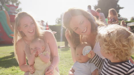 Slow-Motion-Shot-Of-Two-Mothers-Sitting-On-Rug-And-Playing-With-Children-At-Summer-Garden-Fete