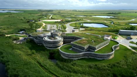 Fast-motion aerial circles modern green-roof wetland centre on a summer day