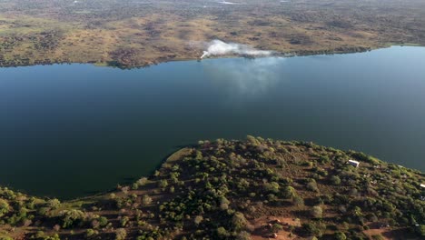 cinematic aerial descending shot of inhampavala lake in chindeguele mozambique during golden hour sunrise with fire on background