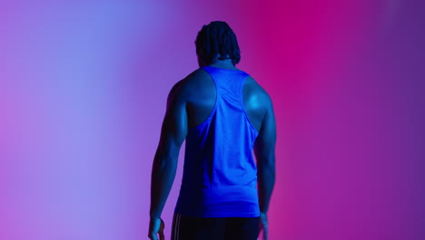 retrato de estudio de vista trasera de un jugador de baloncesto masculino con chaleco de equipo rebotando la pelota contra una iluminación mixta de clave baja colorida