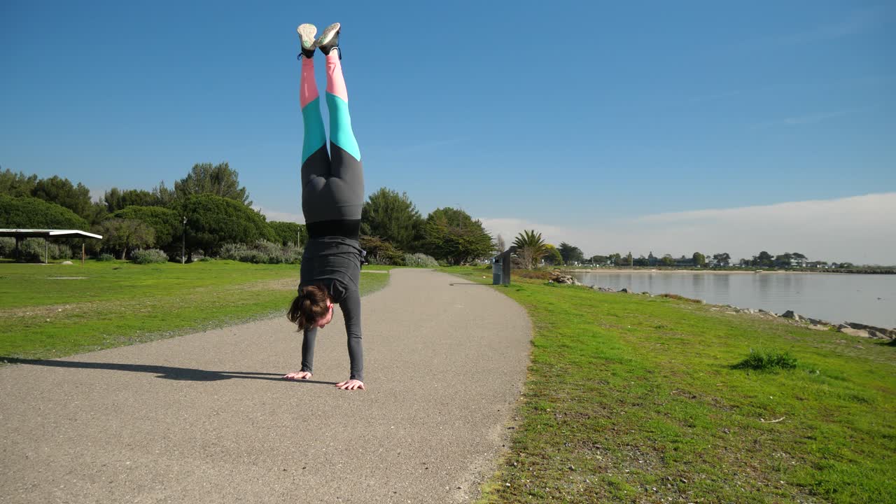 Young athletic girl does a handstand and walks on her hands on pathway