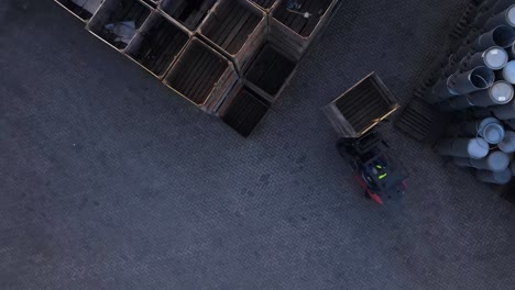 Drone-footage-of-a-forklift-picking-up-pallets-and-loading-them-onto-a-pile-of-stored-pallets-in-a-factory