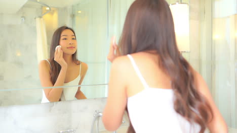 attractive asian woman looking in bathroom mirror checking makeup