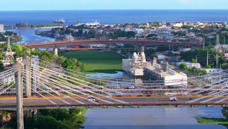 Luftaufnahme-Von-Autos-Auf-Der-Puente-Juan-Bosch-Brücke,-Die-Den-Ozama-Fluss-Mit-Dem-Karibischen-Meer-Im-Hintergrund-überquert