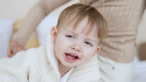 cute smiling caucasian baby boy wearing warm sweater lies on his belly. mom sitting behind tickles her son.