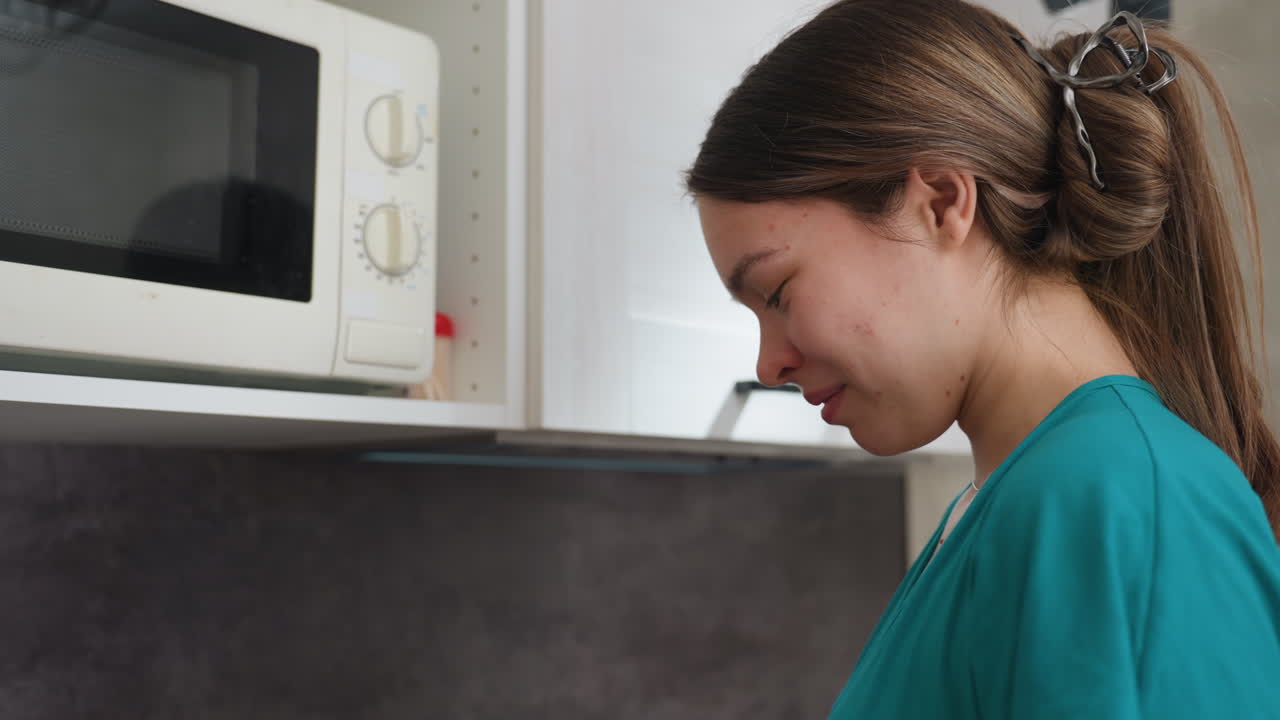 Donna incinta assaggia uno snack al microonde pensierosa, con un cucchiaio vicino alle labbra e al microonde, piccolo assaggio, sorriso sottile ed espressione introspettiva, elettrodomestico da cucina accogliente sullo sfondo, momento consapevole