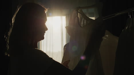 a woman chooses clothes in the dressing room. silhouette in the sun, side view