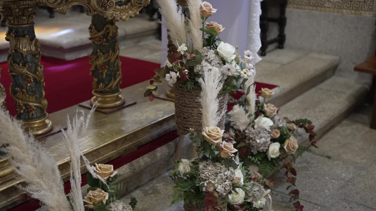 Arranjos florais com flores secas e rosas em cestos de vime, adornando um altar de igreja.