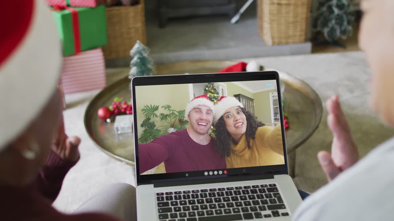 diversas amigas mayores que usan una computadora portátil para una videollamada de navidad con una pareja sonriente en la pantalla