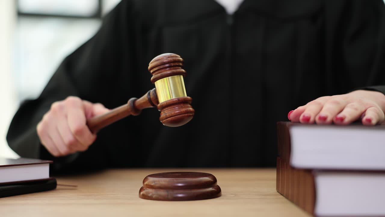 A judge or auctioneer holding a gavel over a sound block with law books on a wooden desk