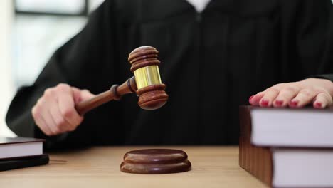 a judge or auctioneer holding a gavel over a sound block with law books on a wooden desk