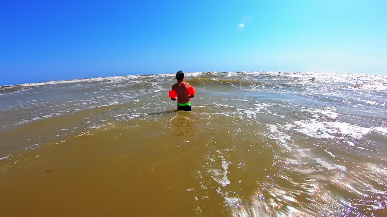 Boy playing in the sea. Bright summer day and small child having fun with foamy waves in the sea water. Slow motion.
