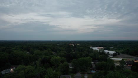 Luftdrohne-Schoss-über-Einer-Kleinen-Stadt,-Die-Während-Der-Abendzeit-Von-Dichter-Vegetation-Umgeben-War