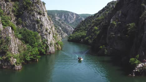 Un-Pequeño-Bote-Con-Turistas-Navega-Entre-Las-Empinadas-Laderas-De-Las-Montañas-Sobre-El-Lago-Matka-En-La-Principal-Atracción-Turística-Matka-Gorge-Del-Norte-De-Marcedonia-En-Un-Día-Soleado-De-Verano