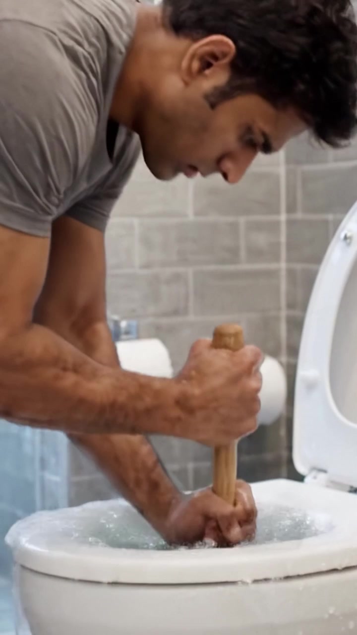 A Man Resolutely Unclogs a Toilet Using a Plunger, Showcasing the Process and Importance of Household Maintenance in a Modern Bathroom Setting