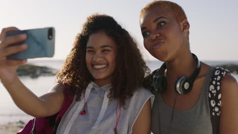 Dos-Amigas-Usando-El-Teléfono-Posando-Para-Selfie-Divirtiéndose-En-La-Playa-Soleada