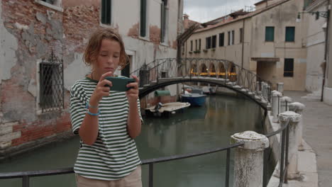 niño con teléfono inteligente cerca del canal veneciano