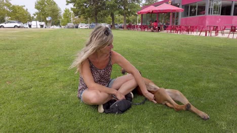 a lady sits outside in the grass at a park with her dog