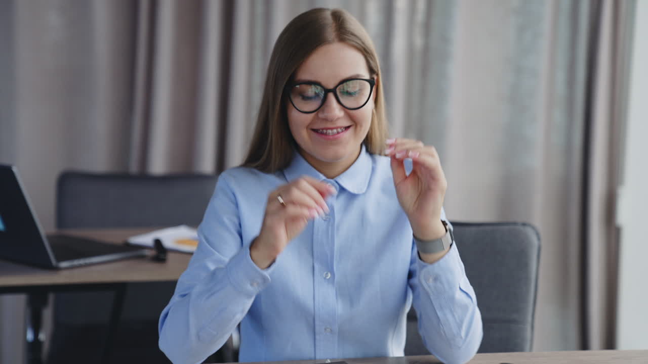 Smiling long-haired woman takes off her glasses. Confident happy business lady in office atmosphere.