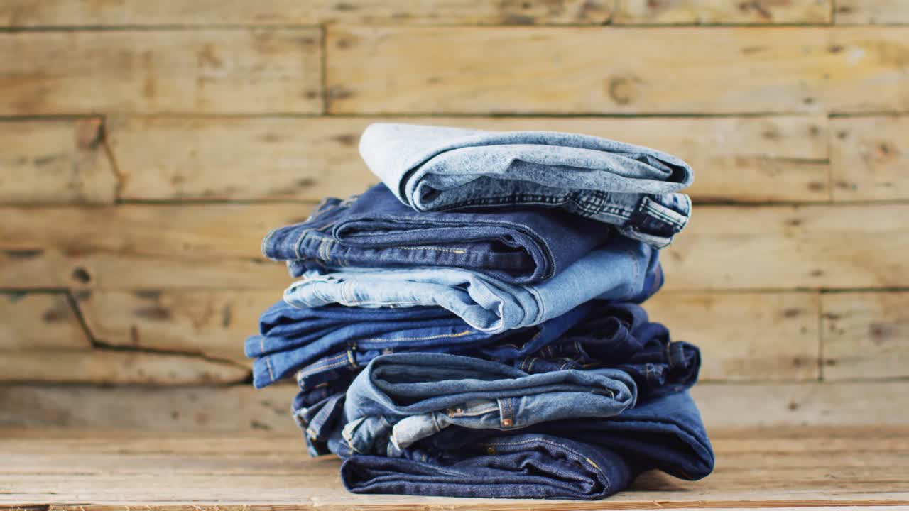 Close up of folded jeans with different shades on wooden background with copy space