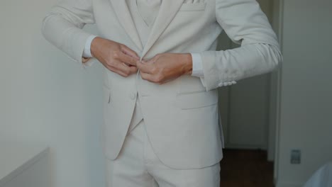 man fastening a light beige coat button, preparing for a formal occasion indoors