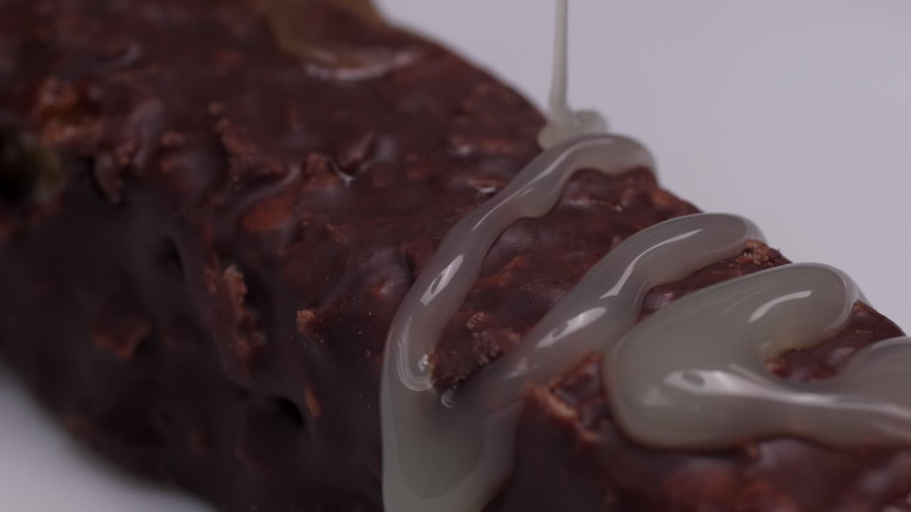 Slow motion macro of condensed milk pouring across over a chocolate bar, rich texture