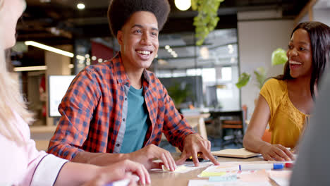 happy diverse colleagues brainstorming with documents and tablet at table in office in slow motion
