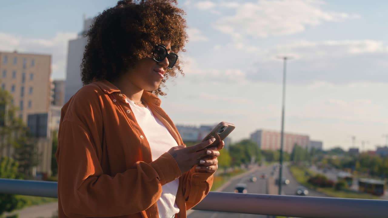 Black woman walking across the bridge and looking at her mobile phone