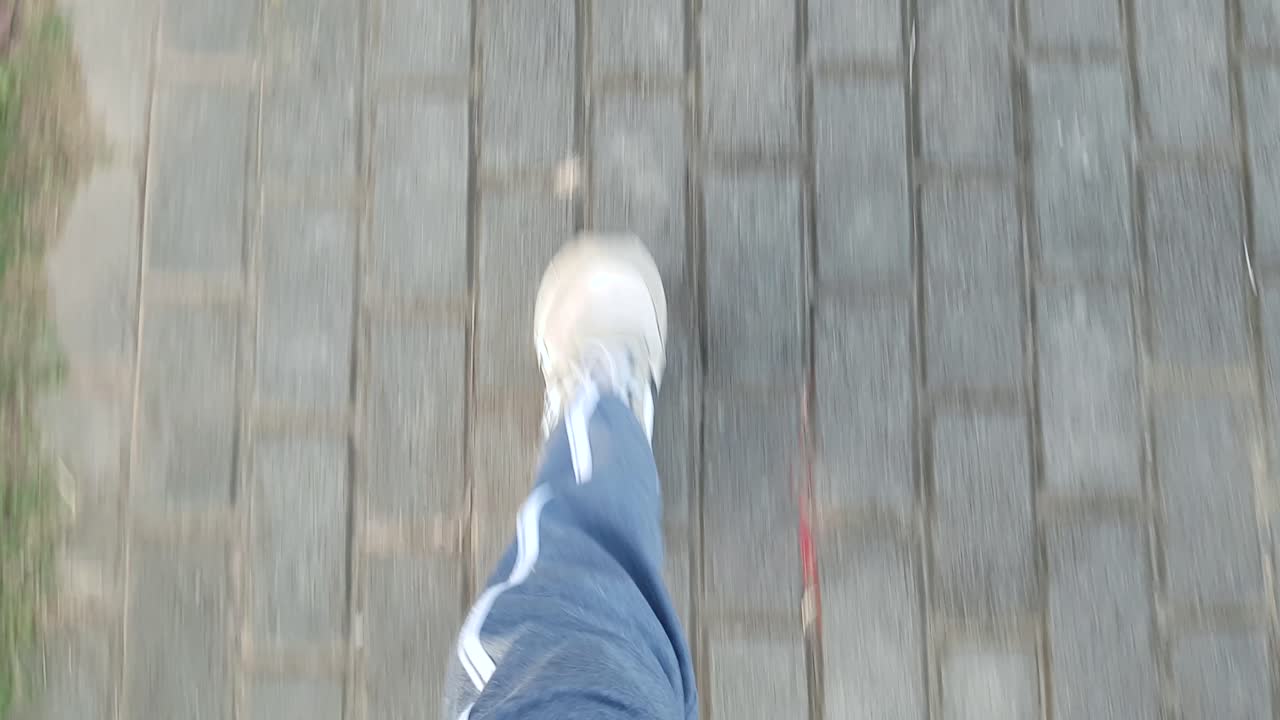 hand held shot of man in white shoes gray sportswear pants walking in a pavement sidewalk view from top waist level