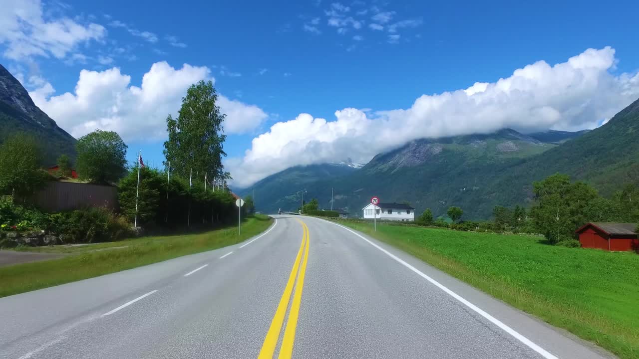 노르웨이의 도로에서 자동차를 운전하고 있습니다. 배경에는 오토바이를 타고 있는 자전거 운전자가 있습니다.