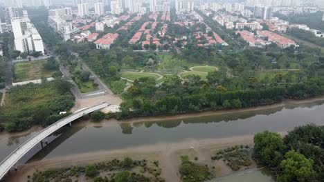 Drone-bird's-eye-view-above-bridge-crossing-river-to-empty-park-in-vietnam-on-foggy-day