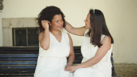 lesbian brides sitting on bench, kissing and holding hands