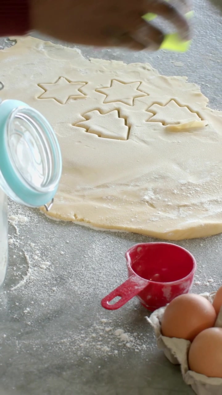 Vertical video: Hand entering pressing cutter in dough for cookies on table burgundy top