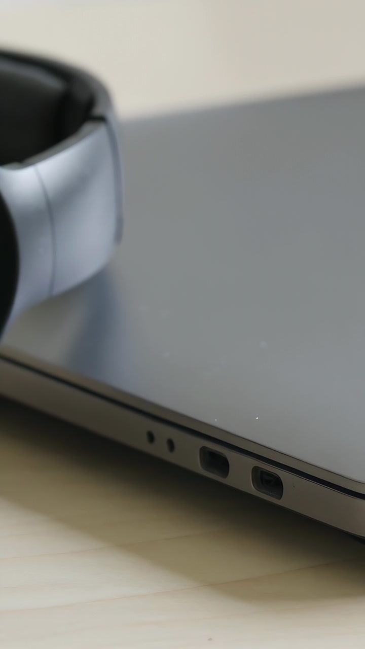 Video verticale: Telecamera panoramica che riprende un laptop chiuso con cuffie su un tavolo luminoso, mettendo a fuoco le porte