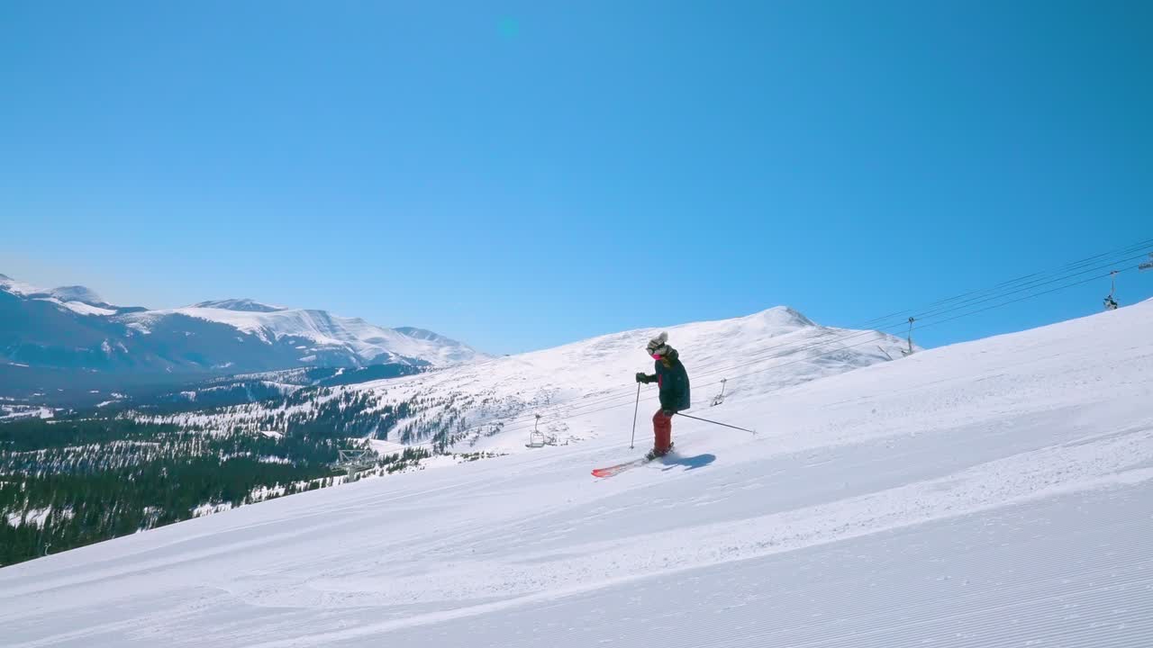 또는 멀리서 산이 있는 은 검은 다이아몬드 스키 경사 아래로 여성 내리막 스키 선수를 추적하는 것