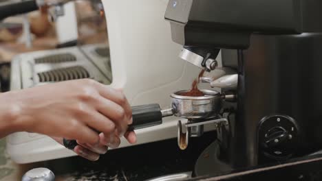 close up of african american female barista preparing coffee at machine in coffee shop, slow motion