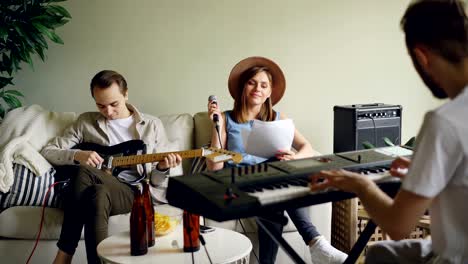 attractive young people musical band are holding rehearsal in room at home, playing musical instruments and singing in microphone. music and millennials concept.