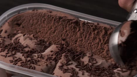 close up view of a person scooping up chocolate ice cream from a tray.