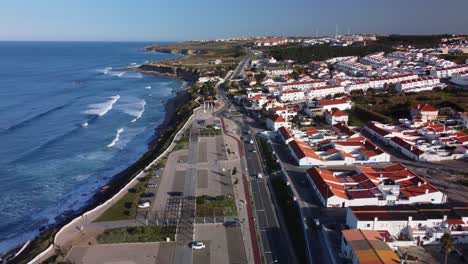 aerial ascending shot of ericeira waterfront houses, ocean waves breaking at the shore