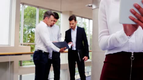 ejecutivas de negocios que usan tabletas digitales mientras sus colegas interactúan en segundo plano