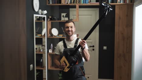 portrait of male cleaner in uniform with vacuum cleaner looking at camera and smiling