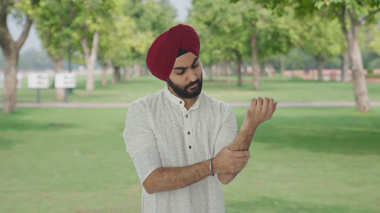 Uomo indiano Sikh malato che soffre di dolore alla mano nel parco